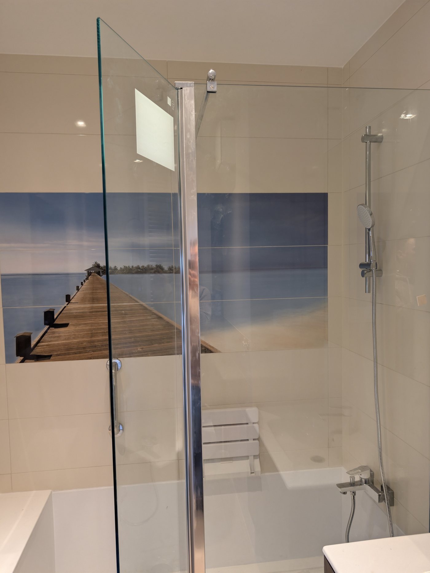 Ta sama łazienka po montażu: prysznic z niskim progiem, szklana ścianka, uchwyt i składane siedzisko